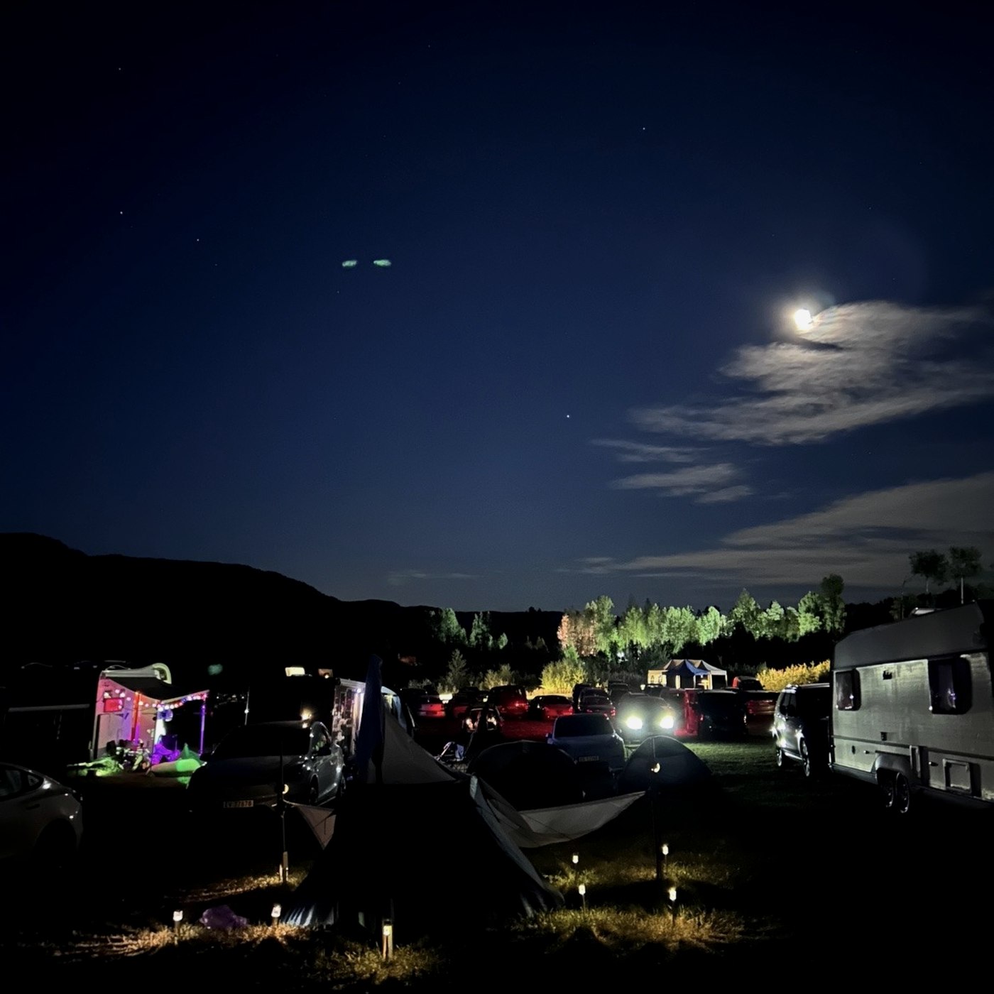 The campsite at night under a bright moon, string lights glowing between tents